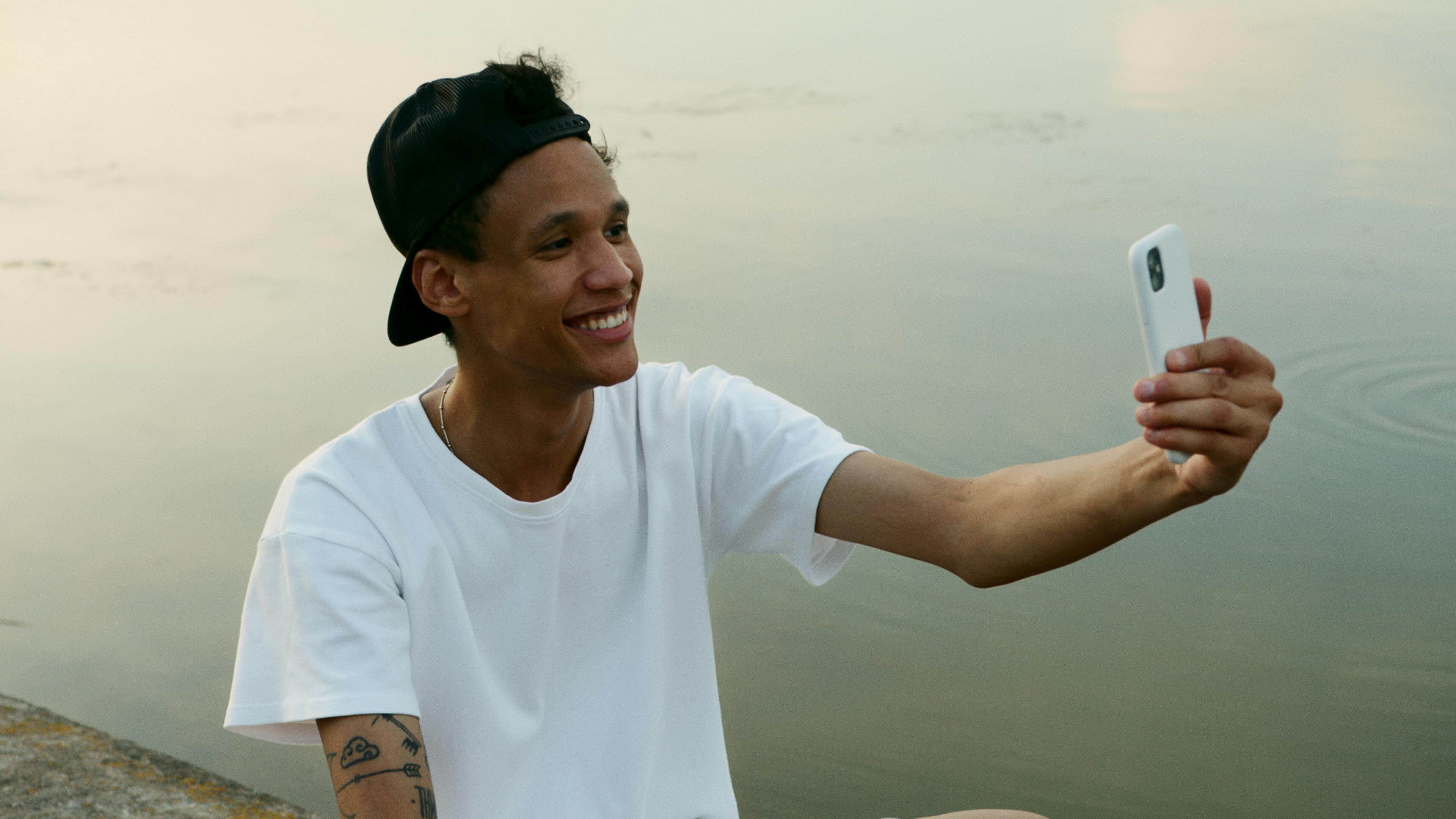 Junger Mann lächelt am See in sein Smartphone